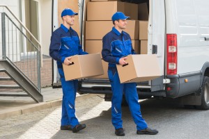 Smiling young delivery men carrying cardboard boxes while walking outside truck